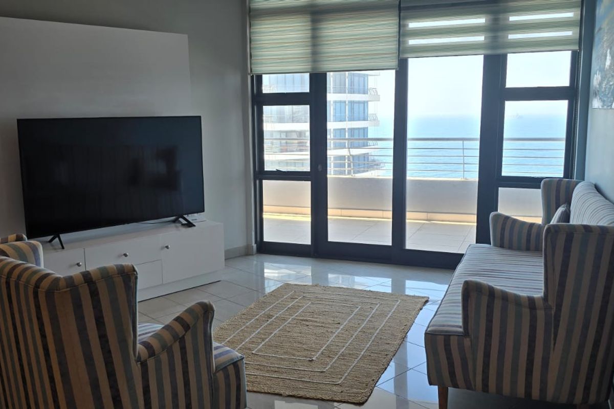 A bright living room featuring tiled floors and large sliding glass doors that provide access to a balcony with ocean views.