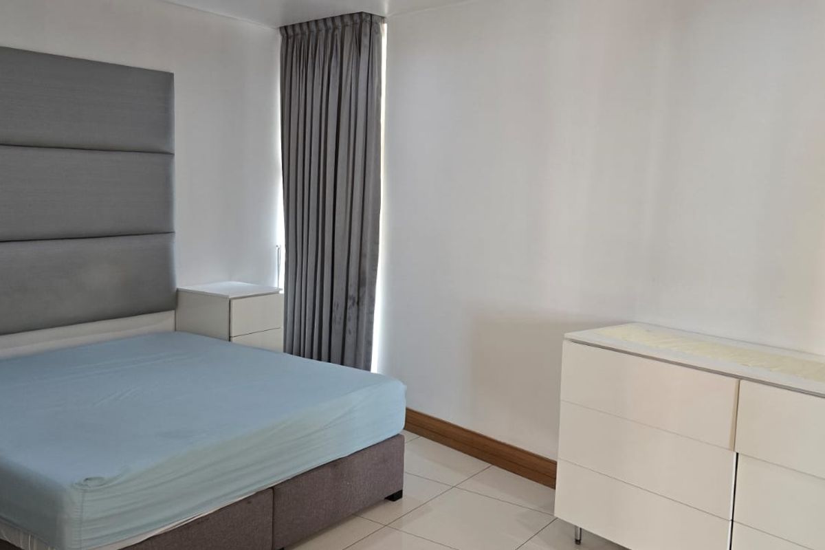 A well-maintained bedroom featuring tiled flooring and a large upholstered headboard, offering a clean and neutral living space.