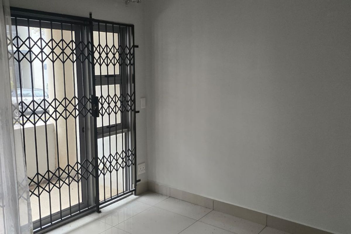 An empty living area featuring tiled flooring, a sliding door with a security gate, and neutral wall finishes.