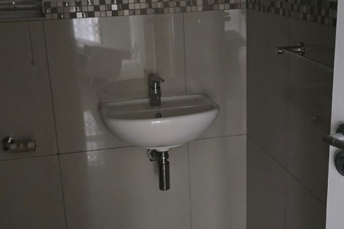 A compact bathroom featuring a wall-mounted basin, chrome fixtures, and tiled finishes, presenting a functional space in need of minor cleaning.