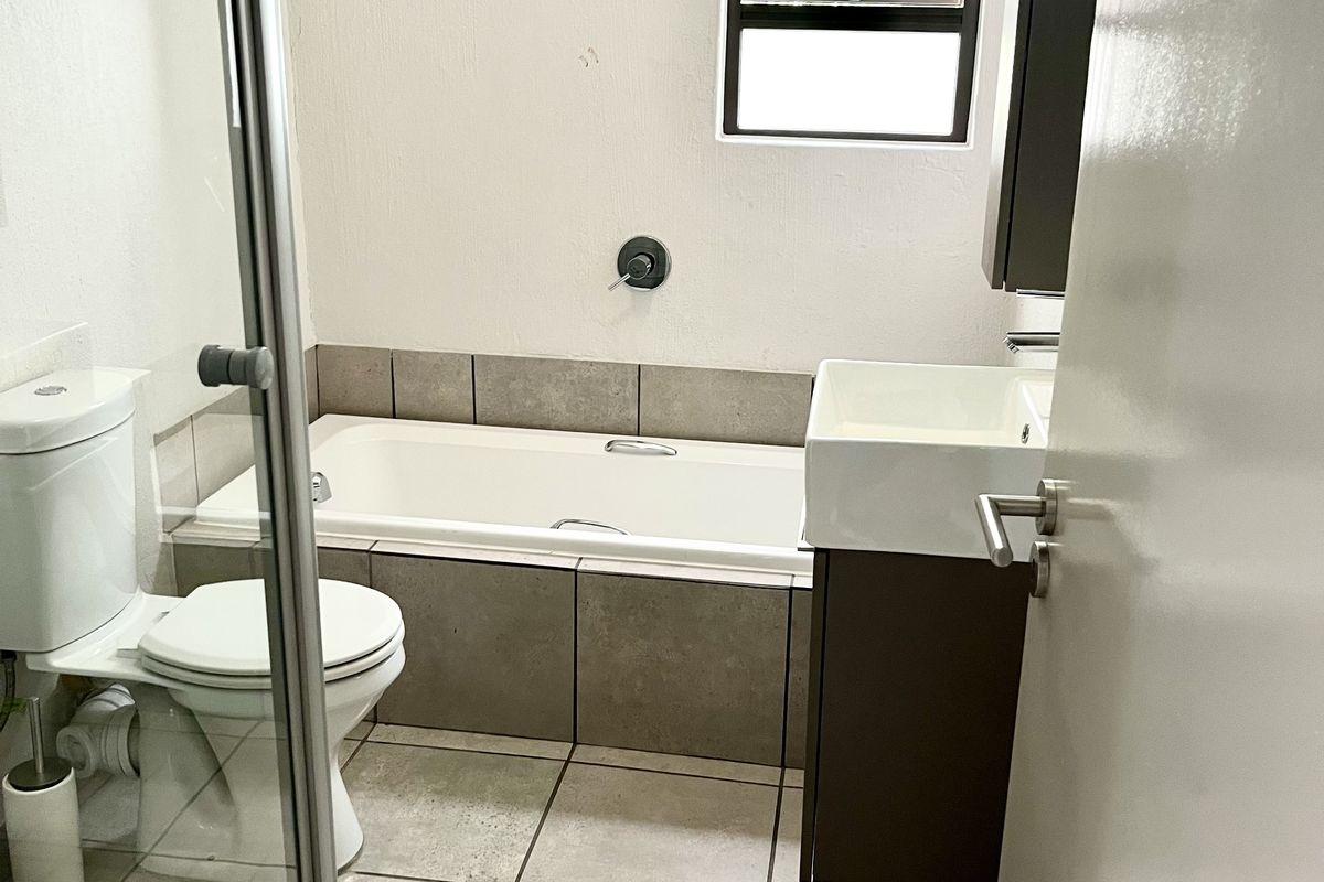 A functional bathroom featuring a built-in bathtub, glass shower enclosure, vanity cabinet with basin, and neutral floor tiling.