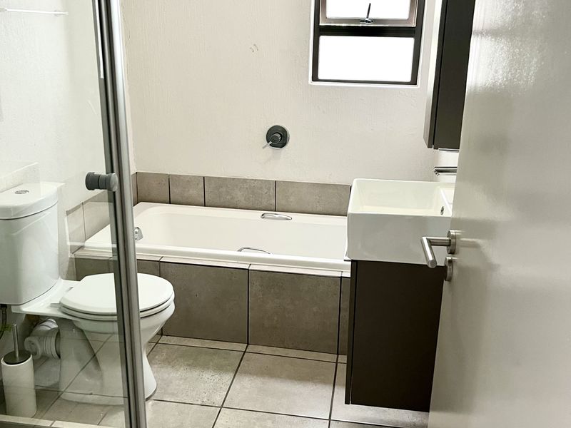 A functional bathroom featuring a built-in bathtub, glass shower enclosure, vanity cabinet with basin, and neutral floor tiling.