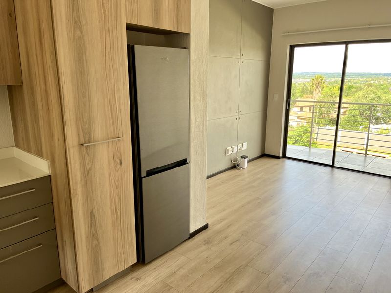 Modern open-plan living area featuring light wood-tone cabinetry, sleek finishes, and a sliding door leading to a balcony with scenic views.
