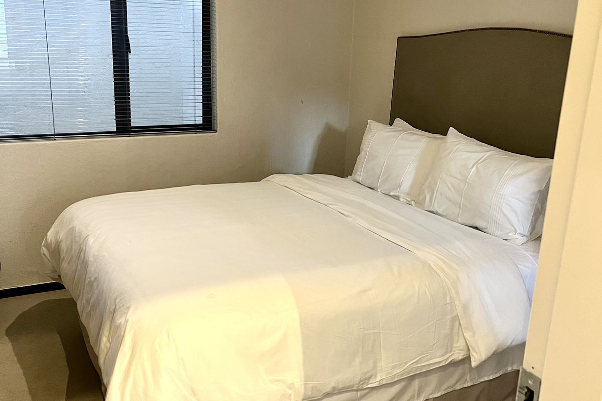 A standard bedroom featuring neutral wall tones, carpeted flooring, and a window fitted with venetian blinds.