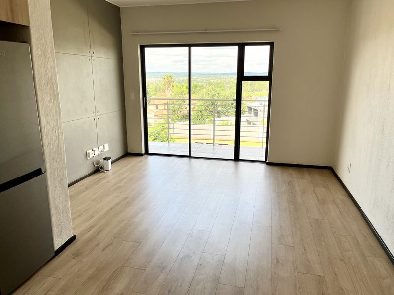 An empty, well-maintained living area featuring light laminate flooring, modern built-in cabinetry, and a large sliding glass door leading to a balcony with views.