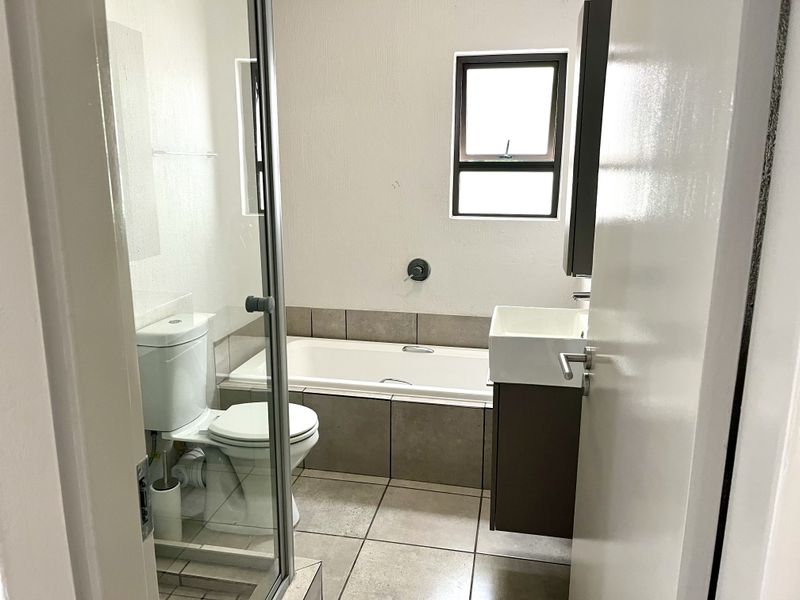 A clean, functional bathroom featuring a built-in bathtub, separate shower enclosure, and a modern wall-mounted vanity with neutral tiling.