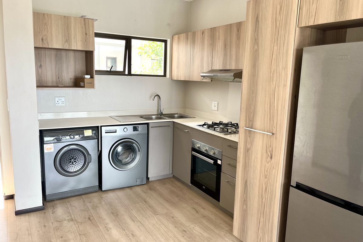 Modern kitchen featuring wood-look cabinetry, stone countertops, integrated gas hob, oven, extractor fan, and dedicated space for laundry appliances.