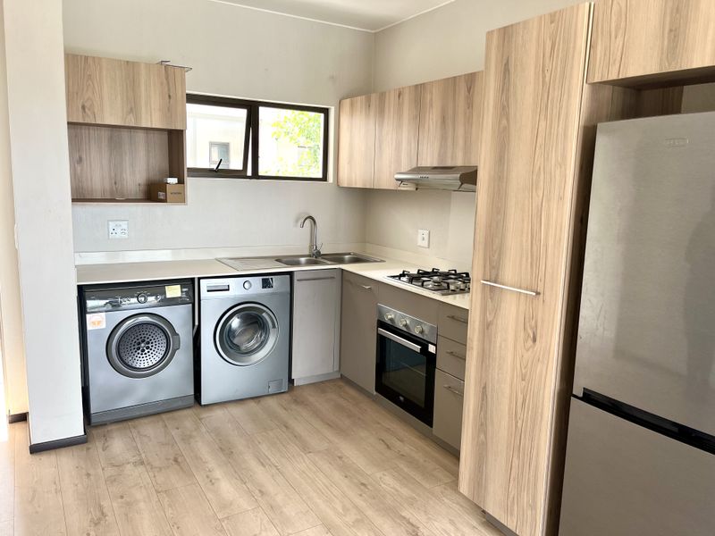 Modern kitchen featuring wood-look cabinetry, stone countertops, integrated gas hob, oven, extractor fan, and dedicated space for laundry appliances.