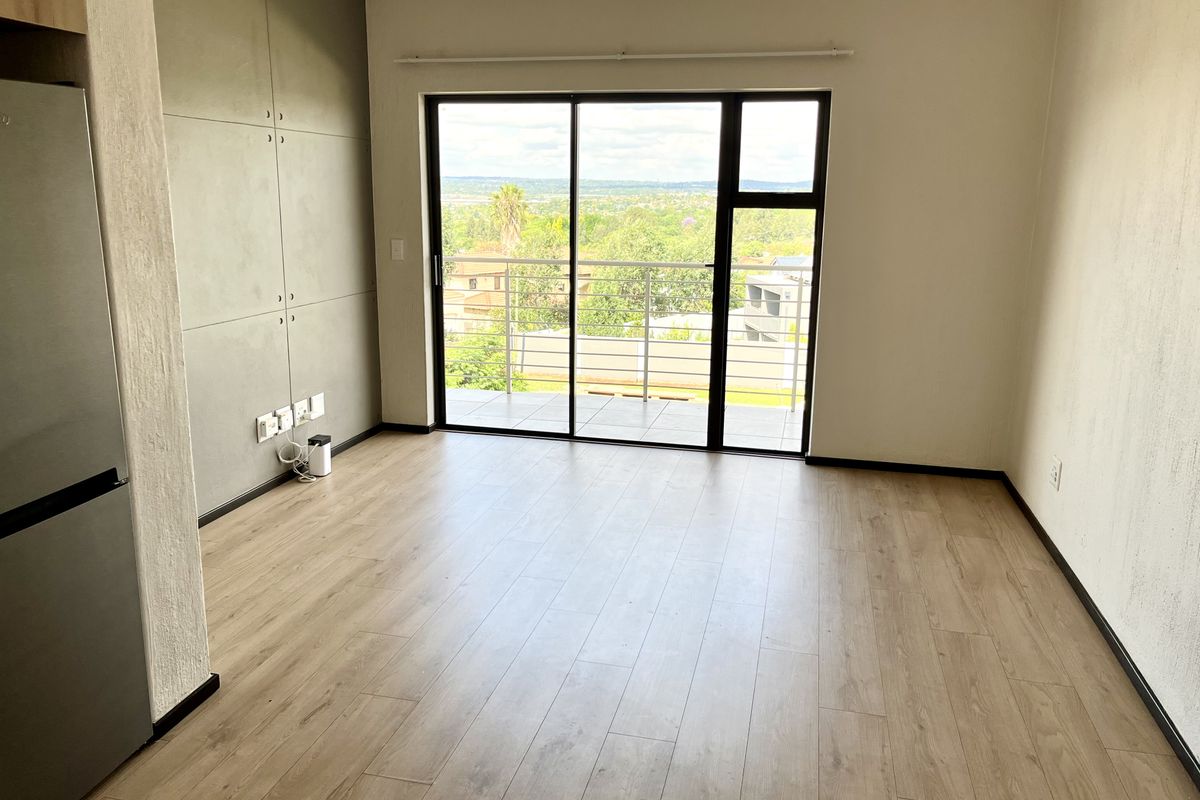 Bright open-plan living area featuring modern laminate flooring, built-in cabinetry, and large sliding glass doors leading to a balcony with scenic views.