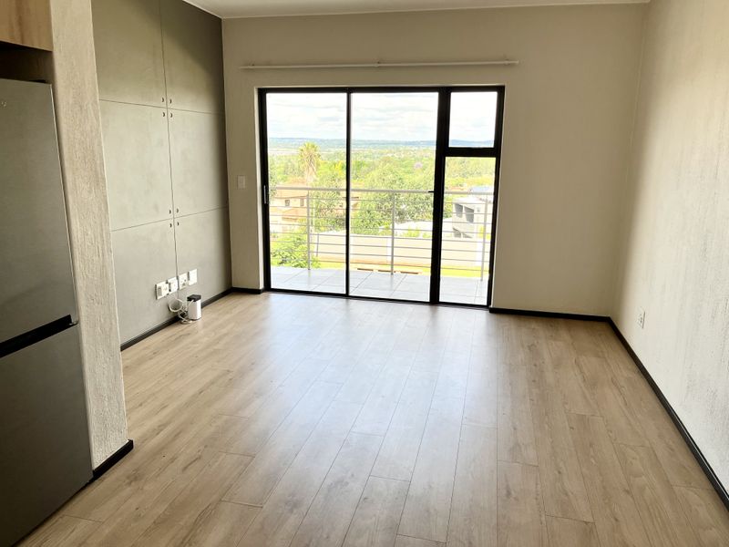 Bright open-plan living area featuring modern laminate flooring, built-in cabinetry, and large sliding glass doors leading to a balcony with scenic views.