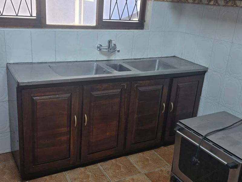A functional kitchen area featuring timber cabinetry, a double bowl stainless steel sink, and tiled splashbacks with a classic design.