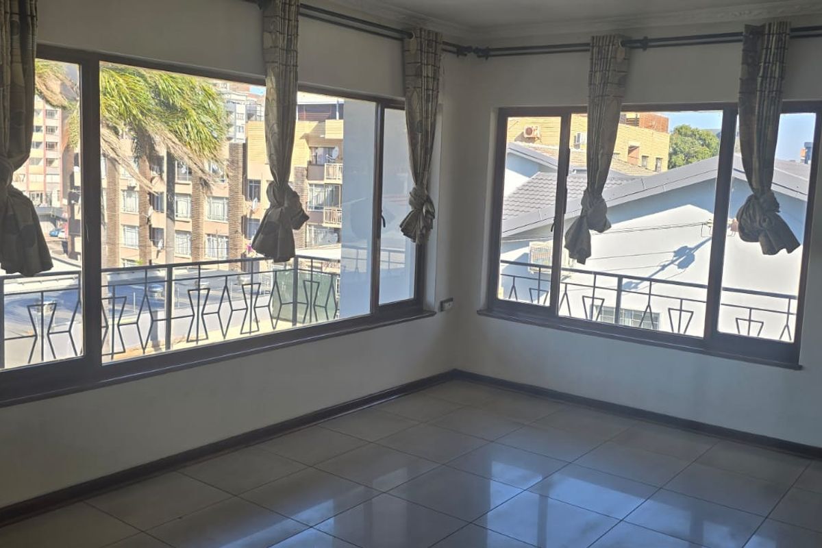 A bright, empty living area featuring large windows with natural light and neutral tiled flooring, offering a versatile space for interior design.