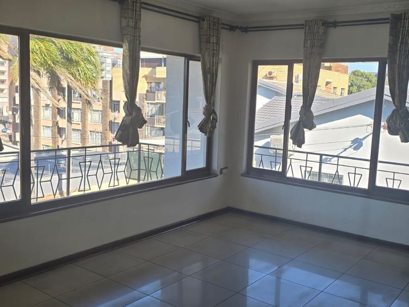 A bright, empty living area featuring large windows with natural light and neutral tiled flooring, offering a versatile space for interior design.