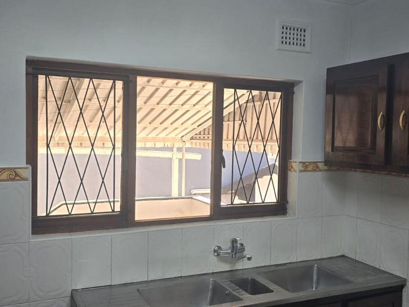A functional kitchen area featuring dark wood cabinetry, a double stainless steel sink, and tiled splashbacks with security-barred windows.