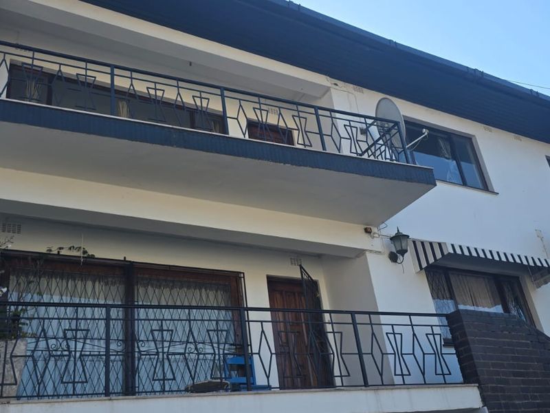Rear elevation of a multi-story house featuring a balcony with wrought iron railings, sliding glass doors, and a brick staircase.