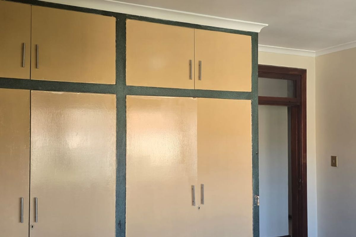 A bedroom featuring floor-to-ceiling built-in cupboards with a dated finish, providing ample storage space within the room.