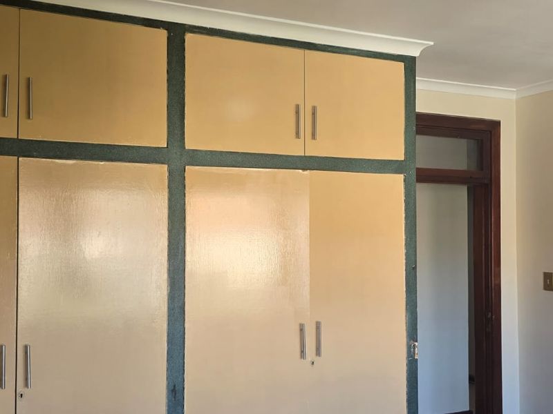 A bedroom featuring floor-to-ceiling built-in cupboards with a dated finish, providing ample storage space within the room.