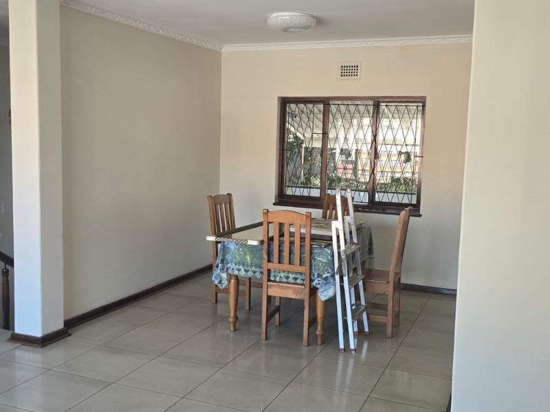 A dining area featuring tiled flooring, a window with security bars, and an adjacent staircase with a wooden balustrade.