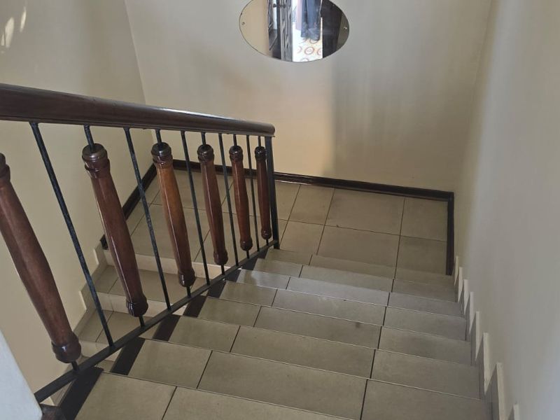 A functional staircase featuring tiled steps, a wooden handrail, and a metal balustrade, providing access between levels.