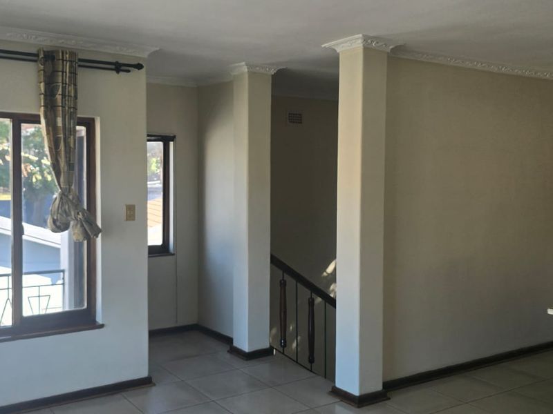 A living area featuring tiled floors, decorative ceiling cornices, and a staircase with a metal balustrade, offering a functional layout with natural light.