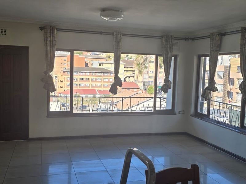 A bright, open-plan living area featuring large windows with urban views, tiled flooring, and neutral wall finishes, offering a blank canvas for interior design.
