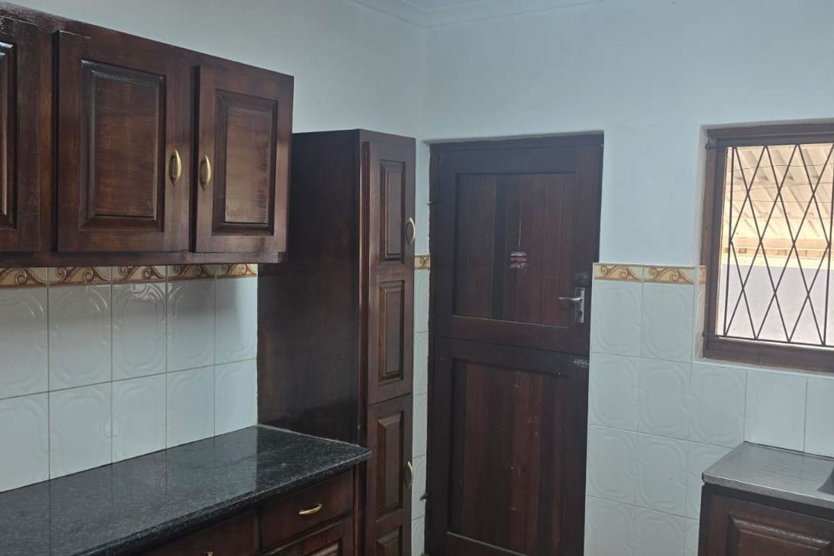 A functional kitchen featuring dark wood cabinetry, granite countertops, a stainless steel sink, and tiled backsplash with a window security gate.