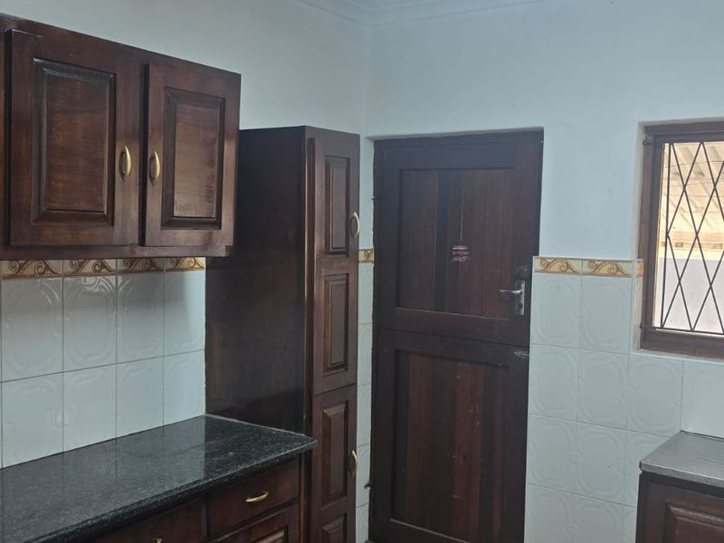A functional kitchen featuring dark wood cabinetry, granite countertops, a stainless steel sink, and tiled backsplash with a window security gate.
