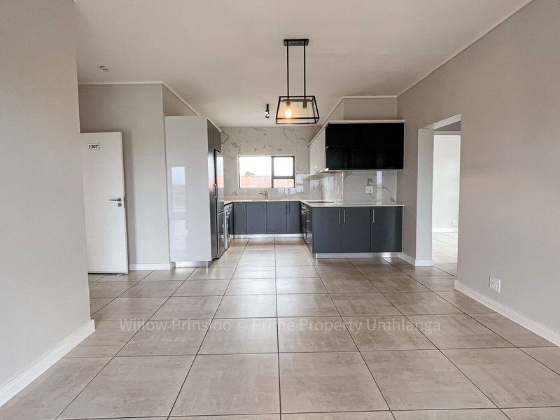 Modern open-plan kitchen and living area featuring sleek cabinetry, marble-look splashbacks, and neutral tiled flooring in a well-maintained apartment setting.