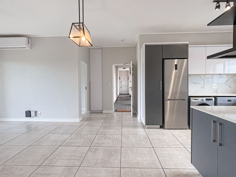 Modern open-plan living area featuring sleek grey and white cabinetry, stone countertops, tiled flooring, and integrated appliances in a bright, contemporary space.