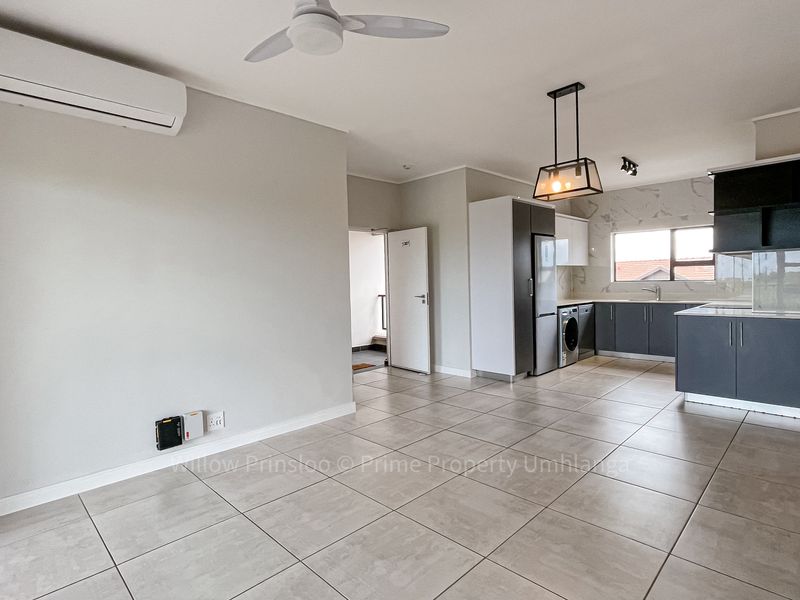 Modern open-plan living area featuring tiled floors, a split-system air conditioner, and a contemporary kitchen with sleek cabinetry and marble-look splashbacks.