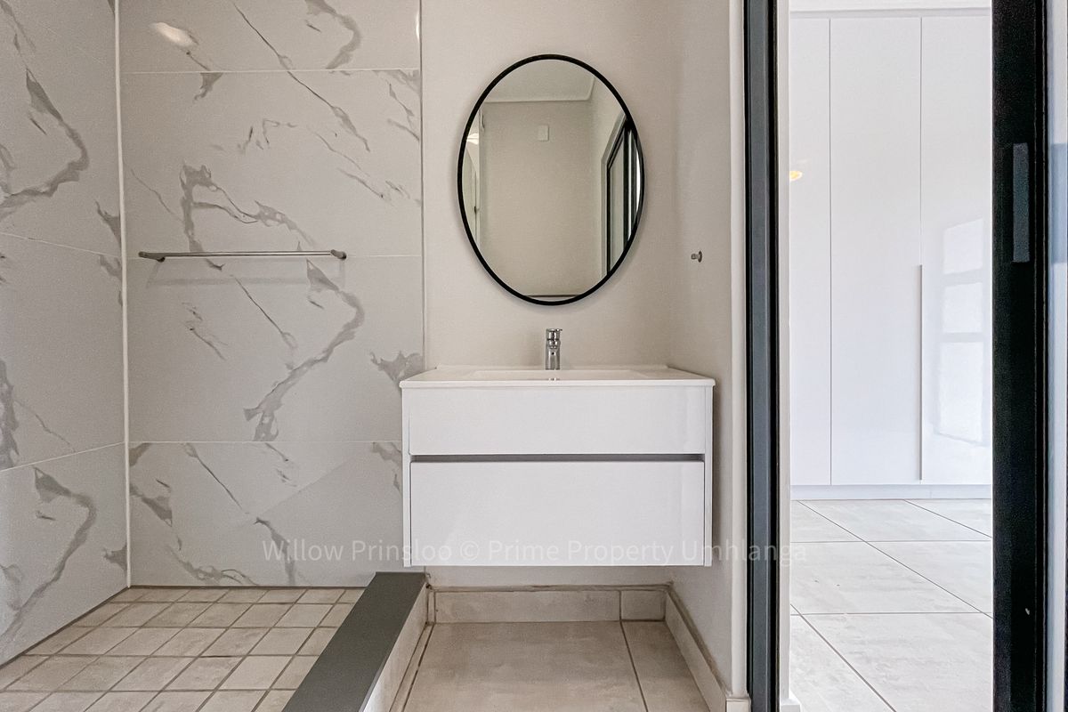 Modern bathroom featuring a floating vanity, marble-look wall tiles, and a walk-in shower, adjacent to a room with built-in cupboards.