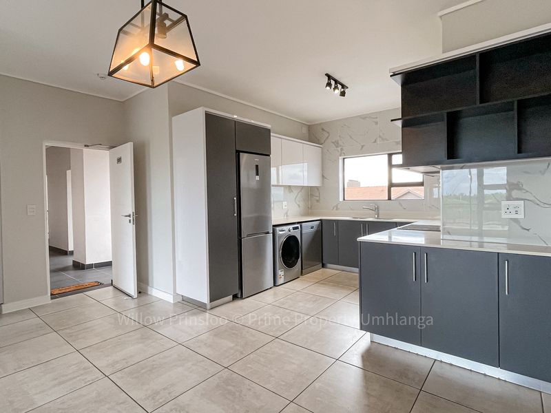Modern kitchen featuring sleek grey and white cabinetry, marble-look splashbacks, integrated appliances, and contemporary lighting fixtures in an open-plan layout.