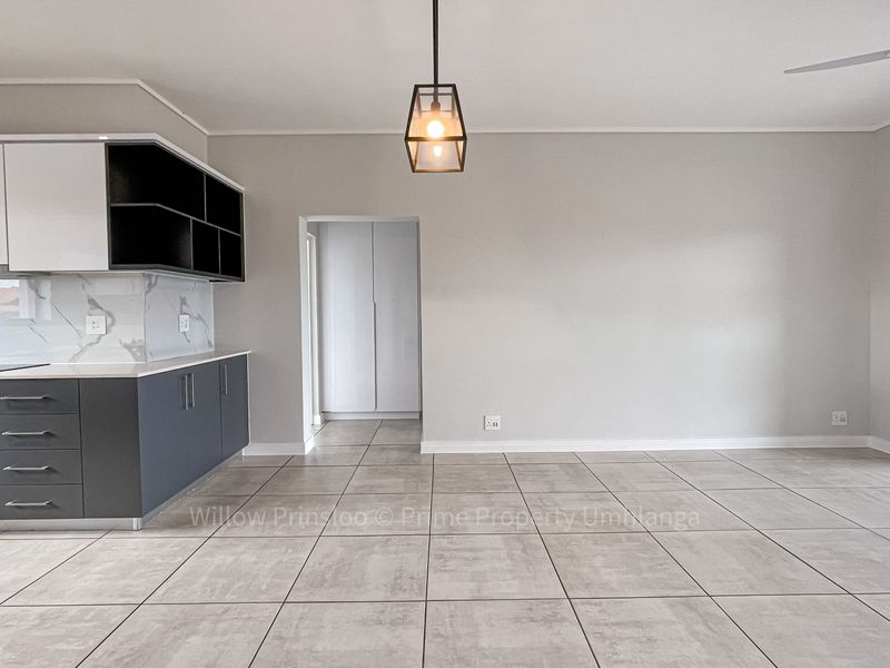 Modern open-plan living area featuring a sleek kitchen with built-in appliances, neutral tiled flooring, and contemporary finishes throughout this bright, vacant apartment space.