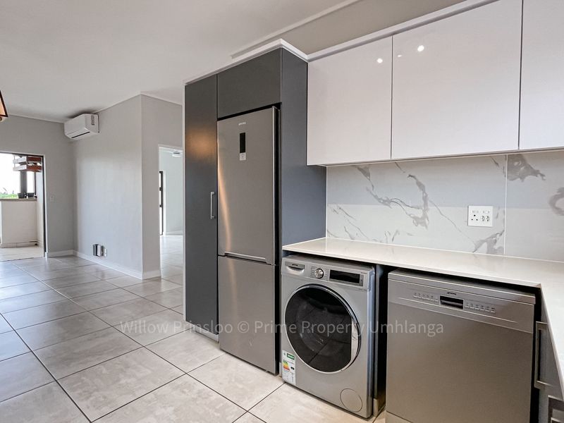 Modern open-plan kitchen and living area featuring sleek cabinetry, stone countertops, marble-look splashback, and direct access to a balcony.