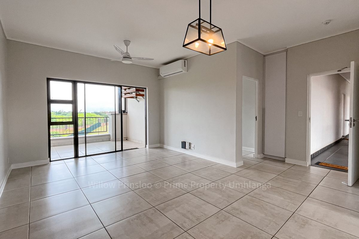 Spacious, light-filled living area featuring neutral tiled flooring, a ceiling fan, air conditioning, and direct access to a private balcony.