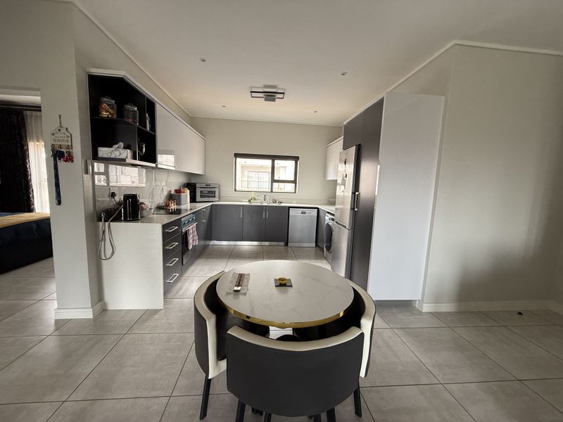 Modern open-plan kitchen featuring sleek two-tone cabinetry, integrated appliances, and tiled flooring, seamlessly flowing into the dining area.