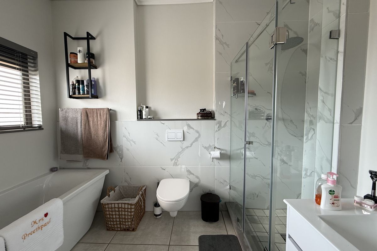 Modern bathroom featuring a freestanding bathtub, a glass-enclosed shower with a rain head, and a wall-mounted toilet with marble-look tiling.