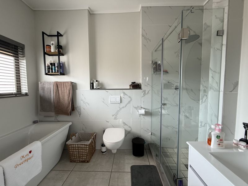 Modern bathroom featuring a freestanding bathtub, a glass-enclosed shower with a rain head, and a wall-mounted toilet with marble-look tiling.