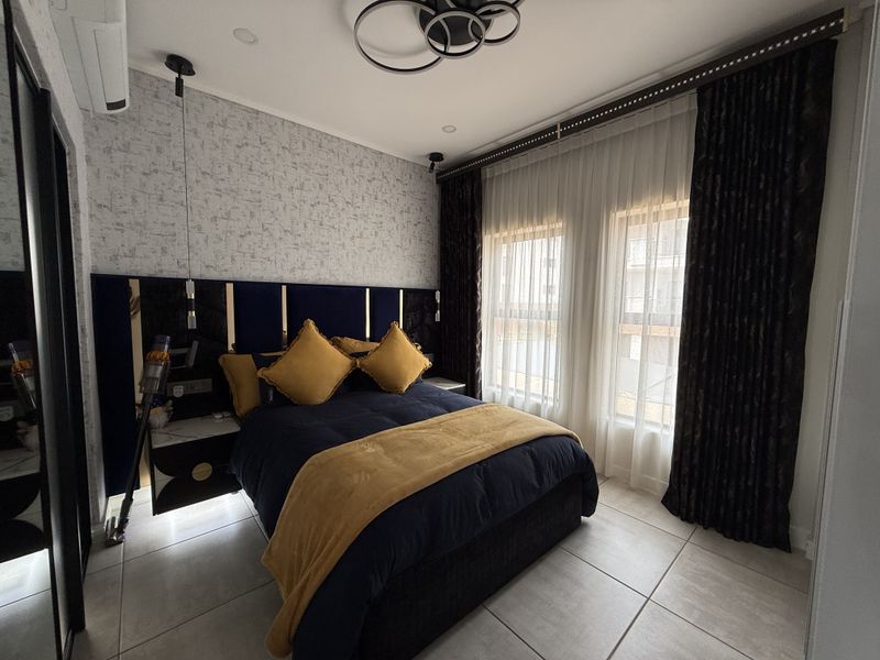 A modern, well-appointed bedroom featuring tiled flooring, recessed ceiling lighting, a split-system air conditioner, and a custom built-in headboard with integrated bedside storage.