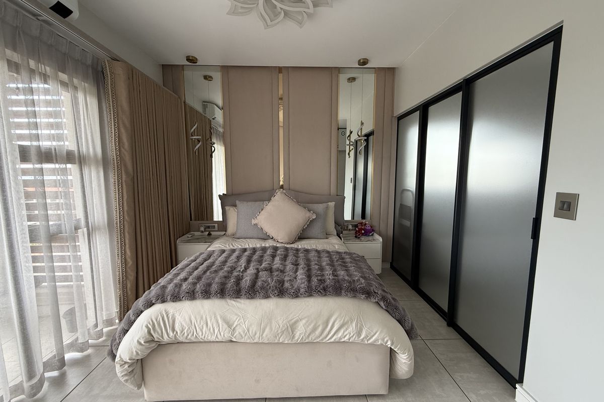 Modern bedroom featuring built-in sliding wardrobes, upholstered wall paneling with integrated mirrors, tiled flooring, and a split-system air conditioner.