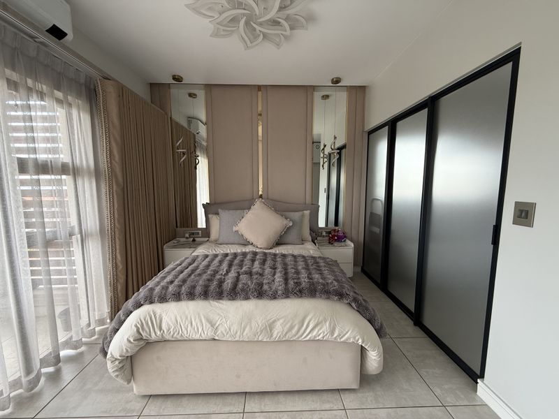 Modern bedroom featuring built-in sliding wardrobes, upholstered wall paneling with integrated mirrors, tiled flooring, and a split-system air conditioner.