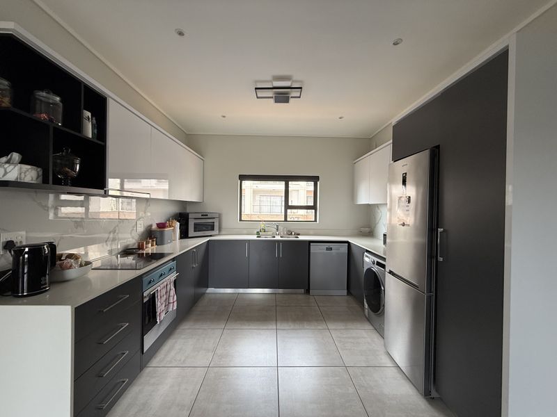 Modern kitchen featuring sleek two-tone cabinetry, stone countertops, integrated appliances, and high-quality tiled flooring in a clean, contemporary layout.