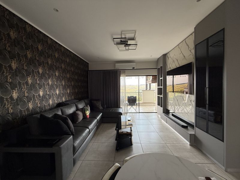 Modern living room featuring tiled floors, a custom built-in media wall with marble-effect paneling, and direct access to a balcony through sliding glass doors.