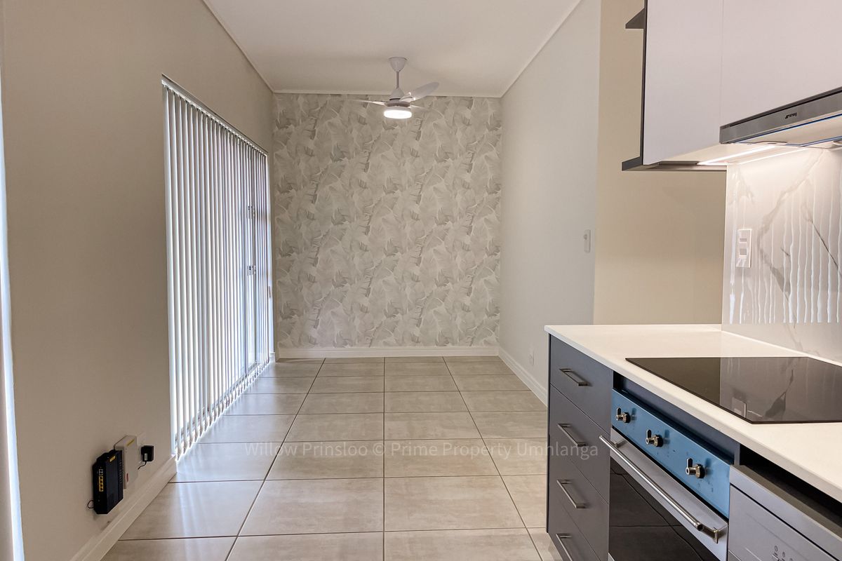 Modern open-plan kitchen and dining area featuring sleek cabinetry, built-in appliances, tiled flooring, and a ceiling fan, leading to a bright patio space.