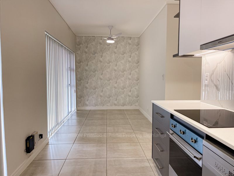 Modern open-plan kitchen and dining area featuring sleek cabinetry, built-in appliances, tiled flooring, and a ceiling fan, leading to a bright patio space.