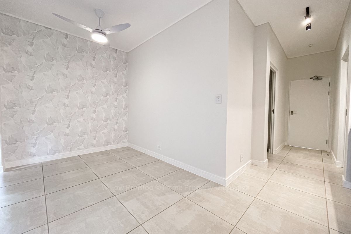 A bright, empty living area featuring neutral tiled flooring, a modern ceiling fan, and a decorative feature wall.