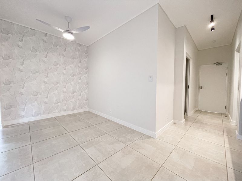 A bright, empty living area featuring neutral tiled flooring, a modern ceiling fan, and a decorative feature wall.