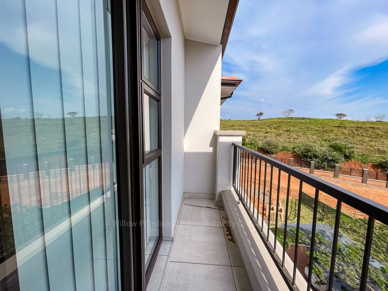 A clean, modern balcony featuring tiled flooring and a metal balustrade, offering an open view of the surrounding landscape.