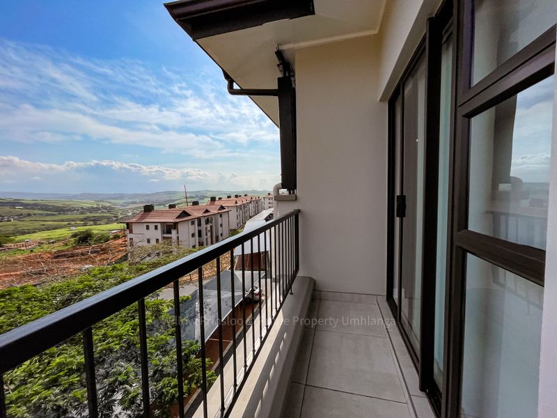 A clean, modern balcony featuring tiled flooring, a secure metal balustrade, and sliding glass doors, offering expansive views of the surrounding landscape.