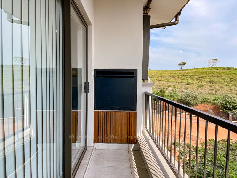 A clean, modern balcony featuring a built-in braai, metal balustrade, and tiled flooring, offering an open view of the surrounding landscape.